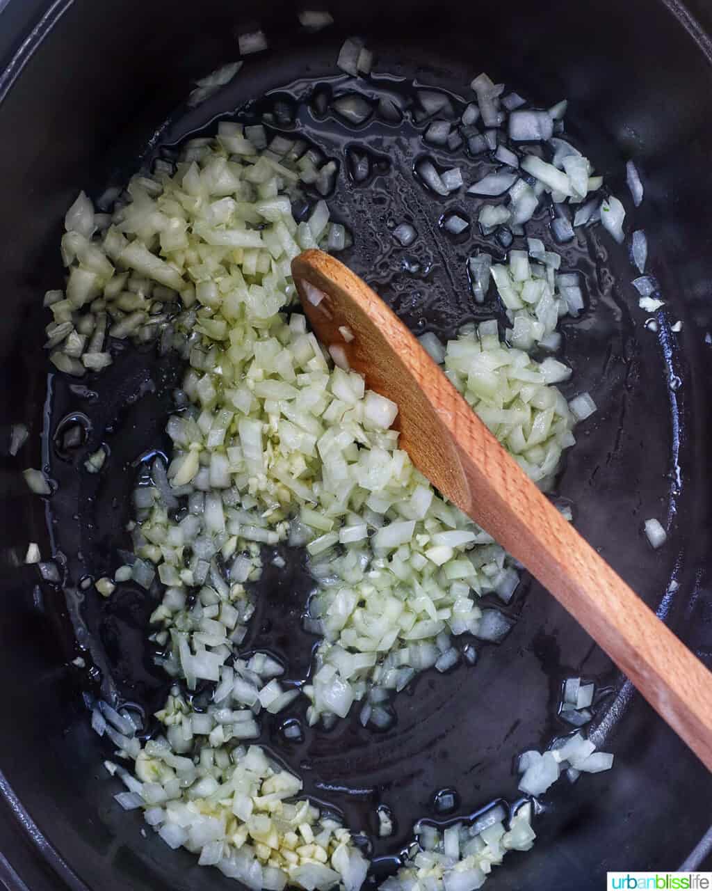 wooden spoon stirring onions and garlic in a Dutch oven.