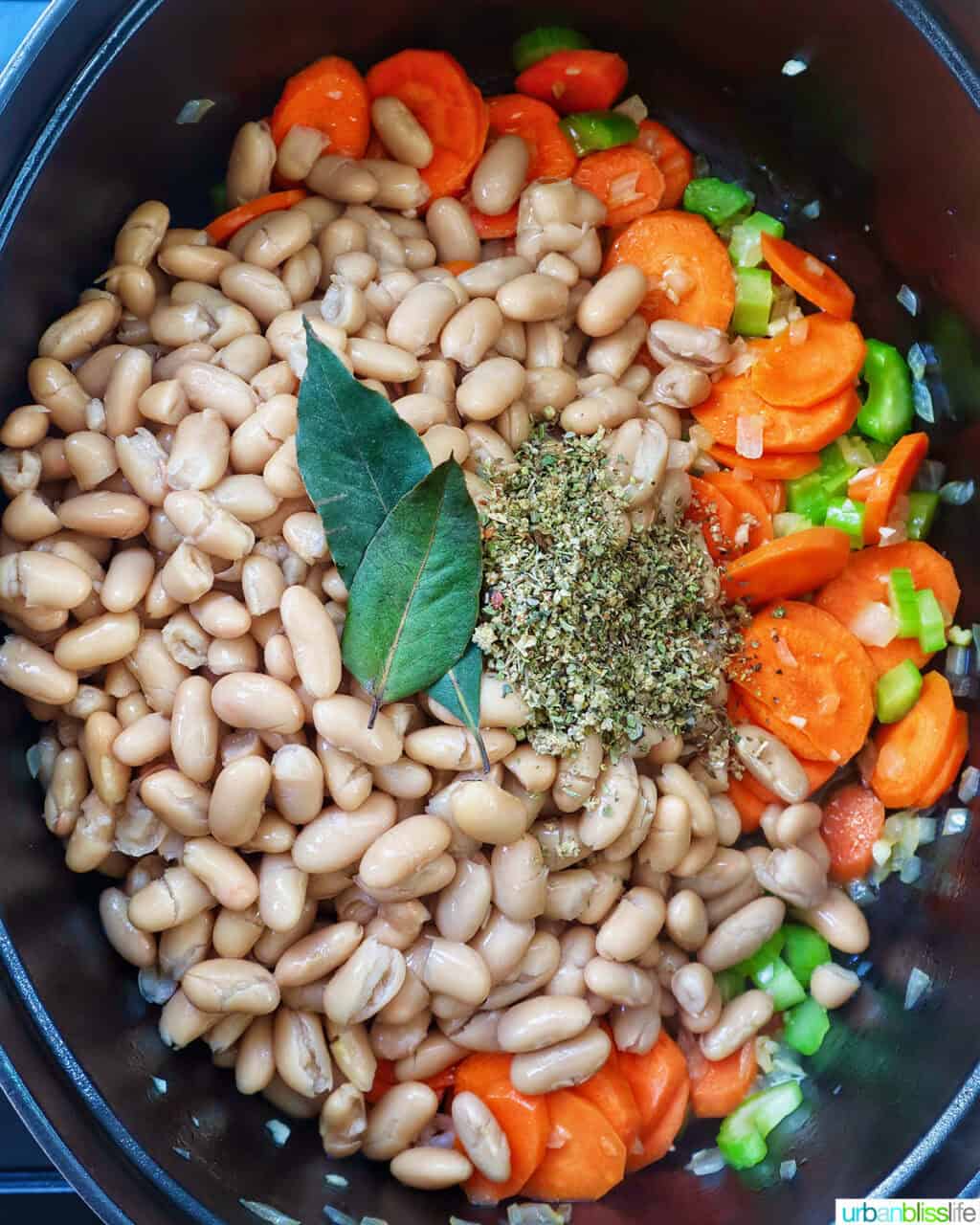 beans, bay leaves, and herbs added to carrots, celery, onions, and garlic to make tuscan kale soup.
