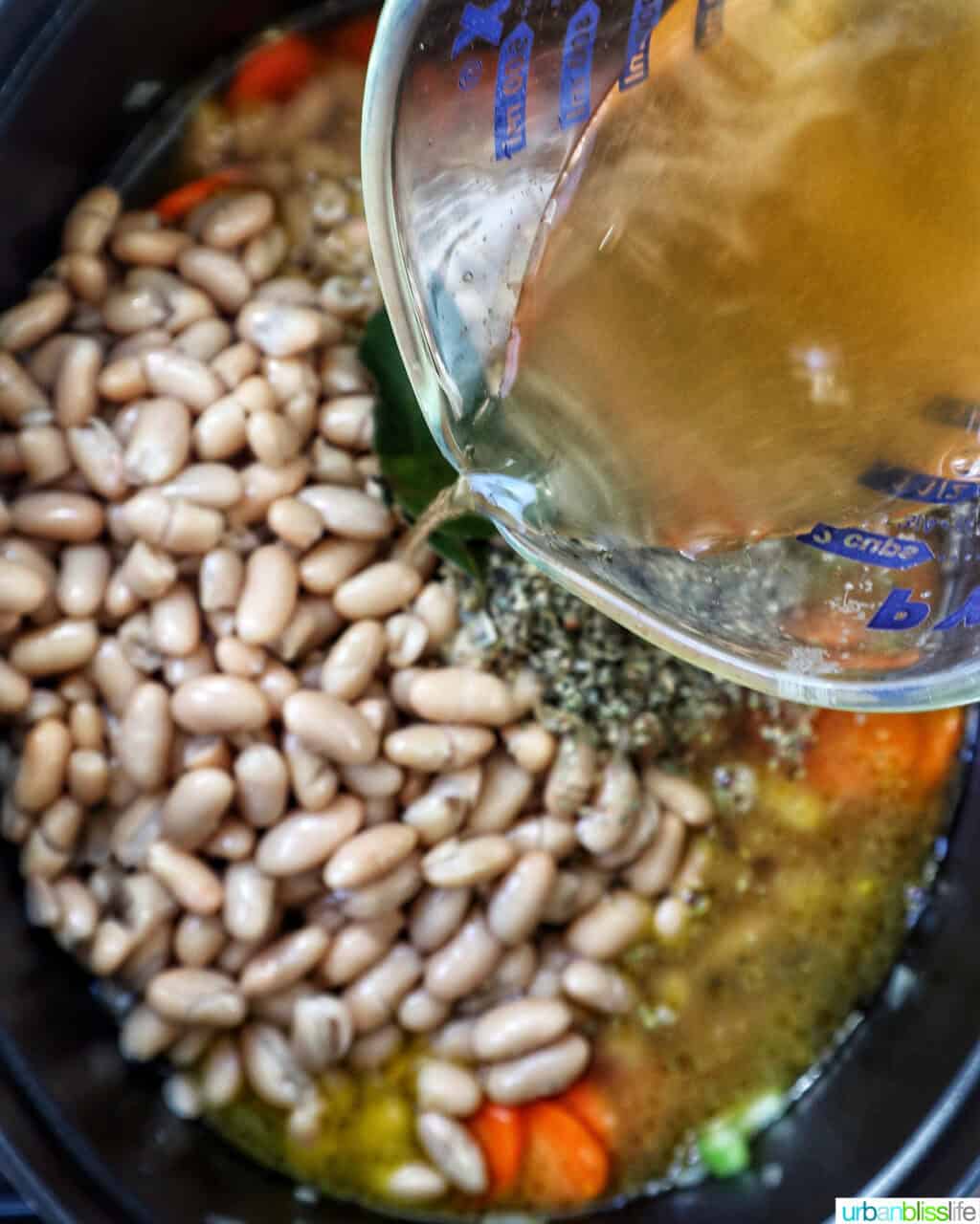 vegetable broth being added to Tuscan kale and white bean soup in a Dutch oven.
