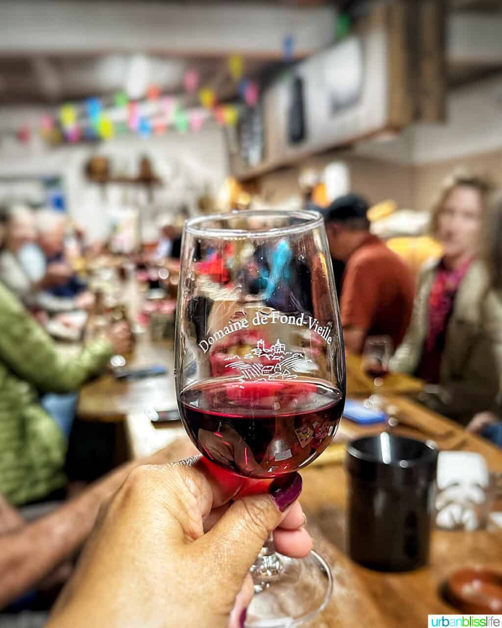 glass of red wine with group wine tasting in the background in Beaujolais, France.