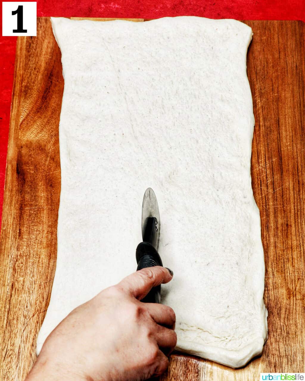using a pizza cutter to slice refrigerated pizza dough.