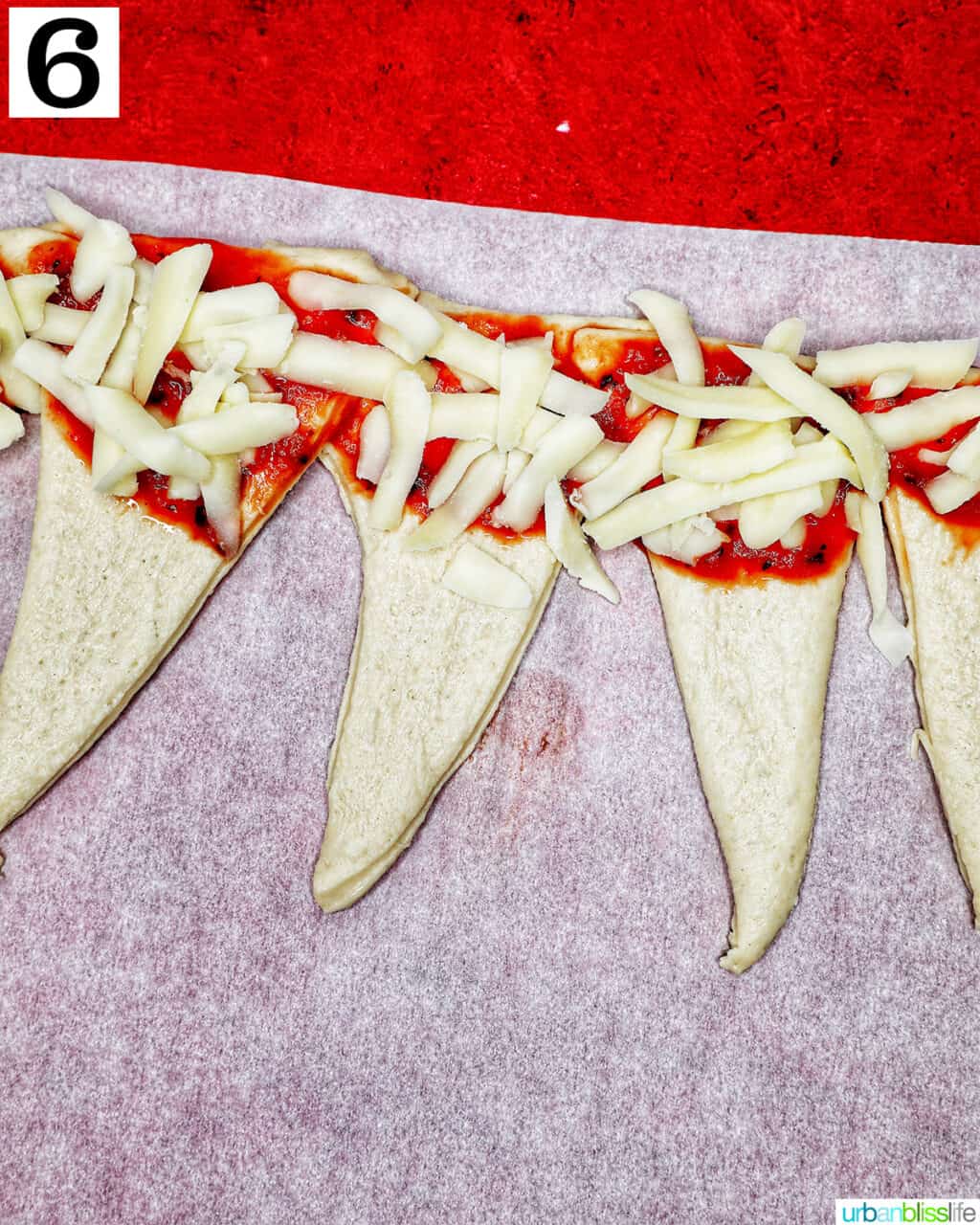 adding shredded cheese onto pizza sauce on triangles of pizza dough.