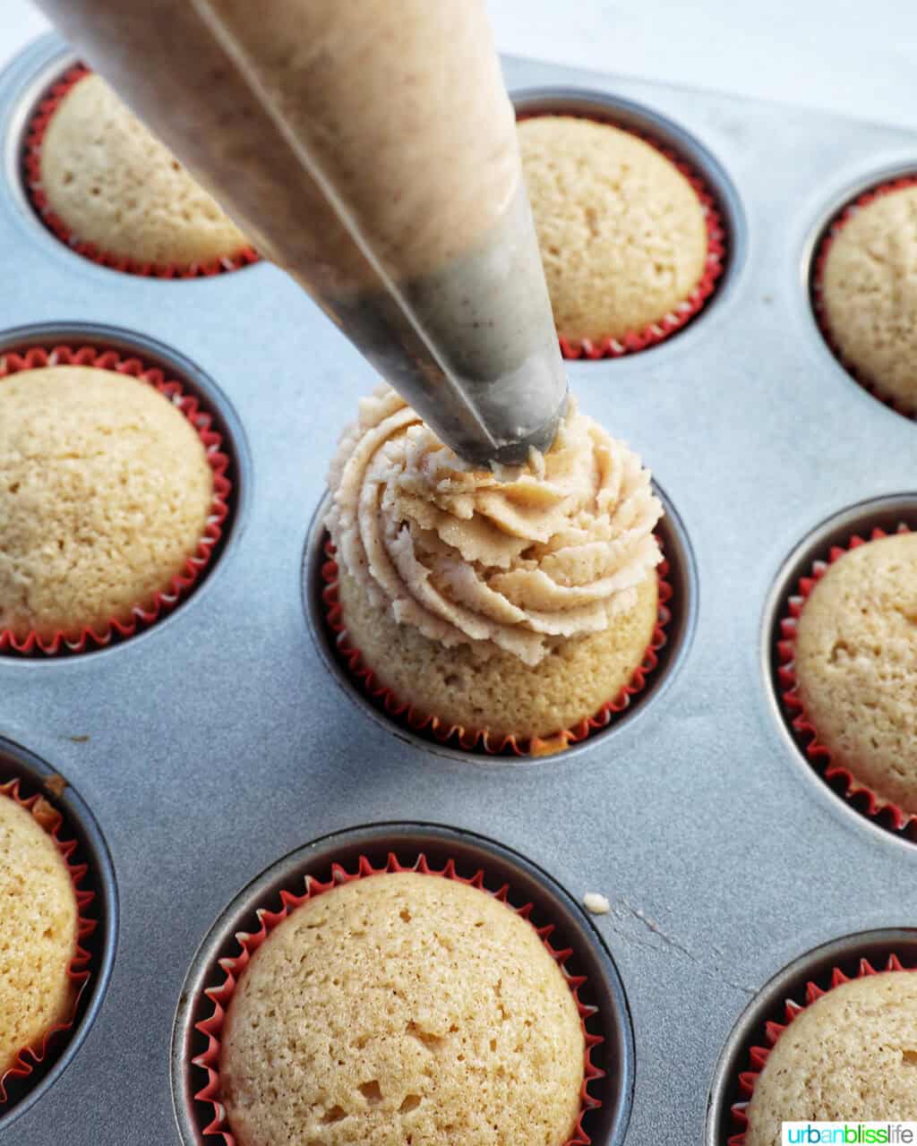 piping bag piping cinnamon frosting onto cupcakes.