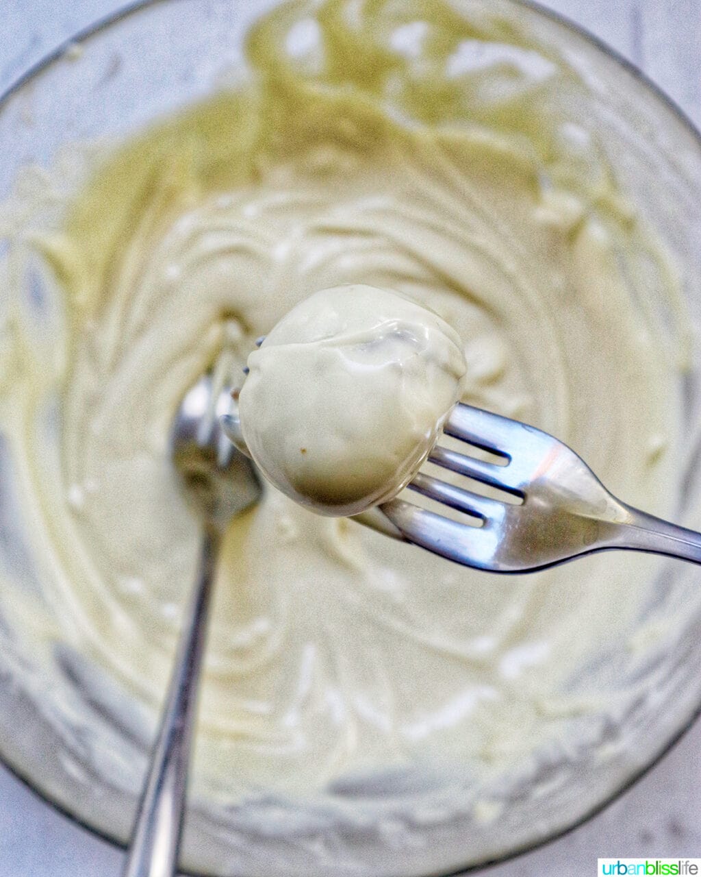 two forks dipping a truffle into a bowl of melted white chocolate.