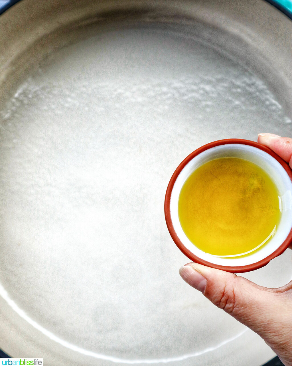 hand holding bowl of olive oil over pan.