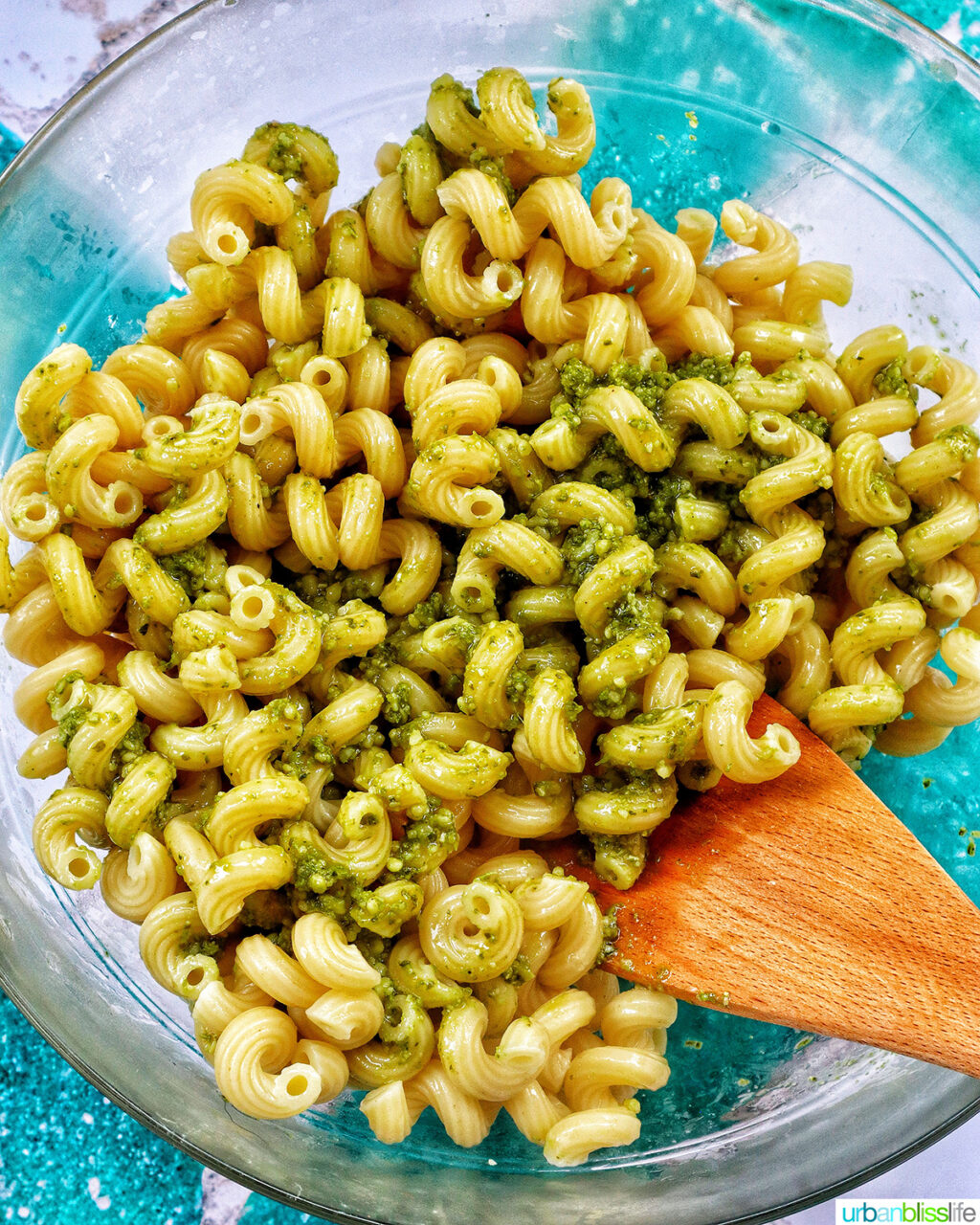 wooden spoon in bowl with pasta and pesto sauce.