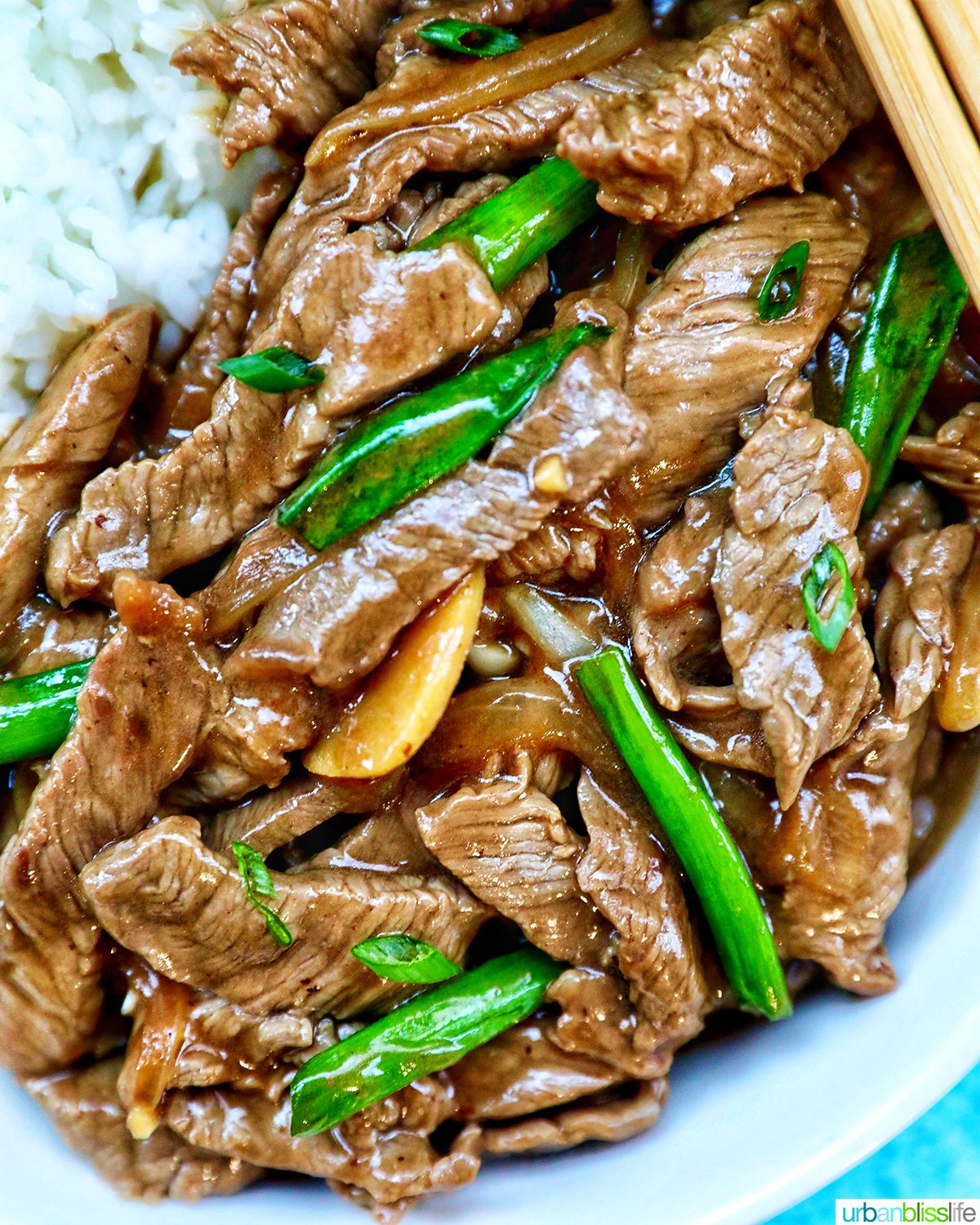 bowl of beef and onion stir fry with white rice and chopsticks.