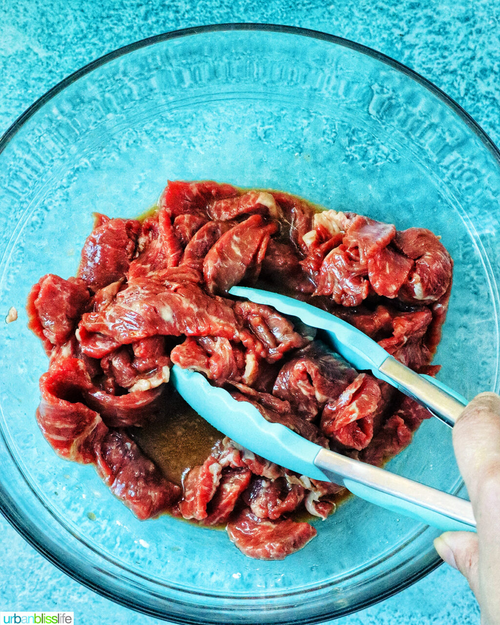 tongs with sliced beef in a bowl.