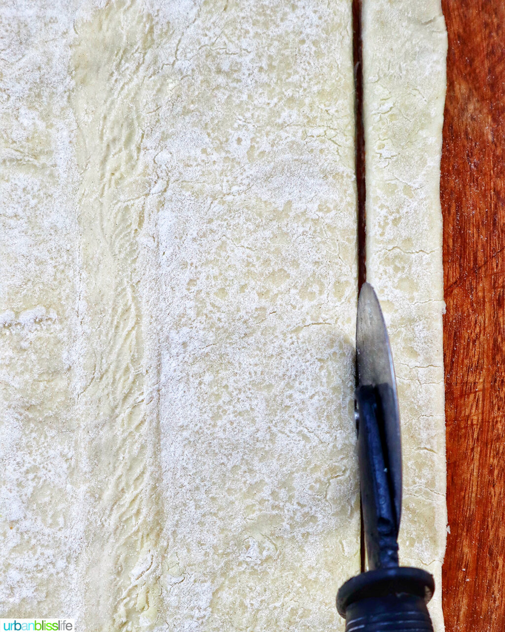 pizza cutter cuting strips of puff pastry on a cutting board.