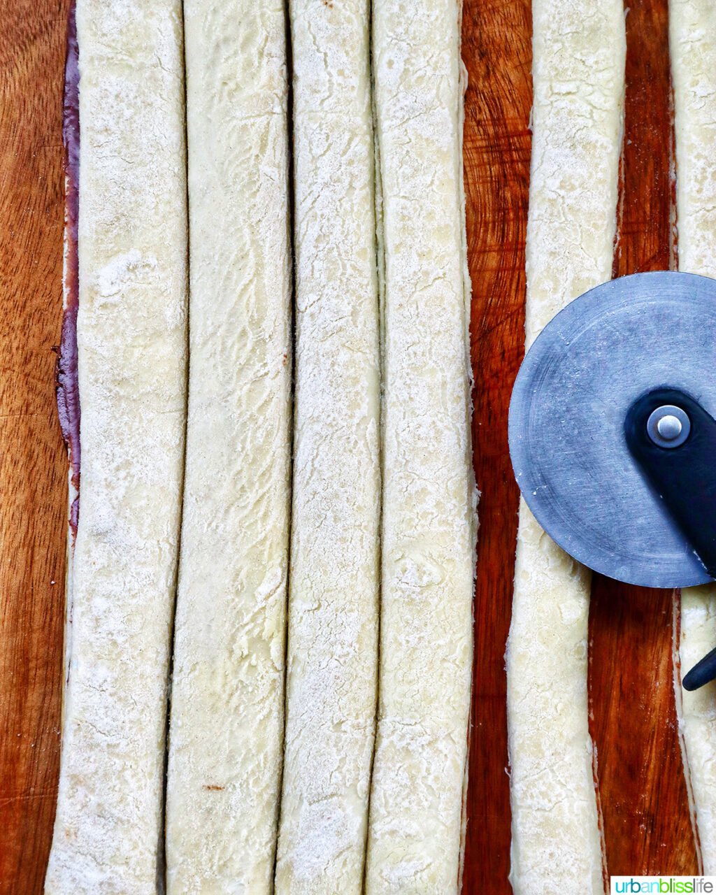 pizza cutter with strips of puff pastry on a cutting board.