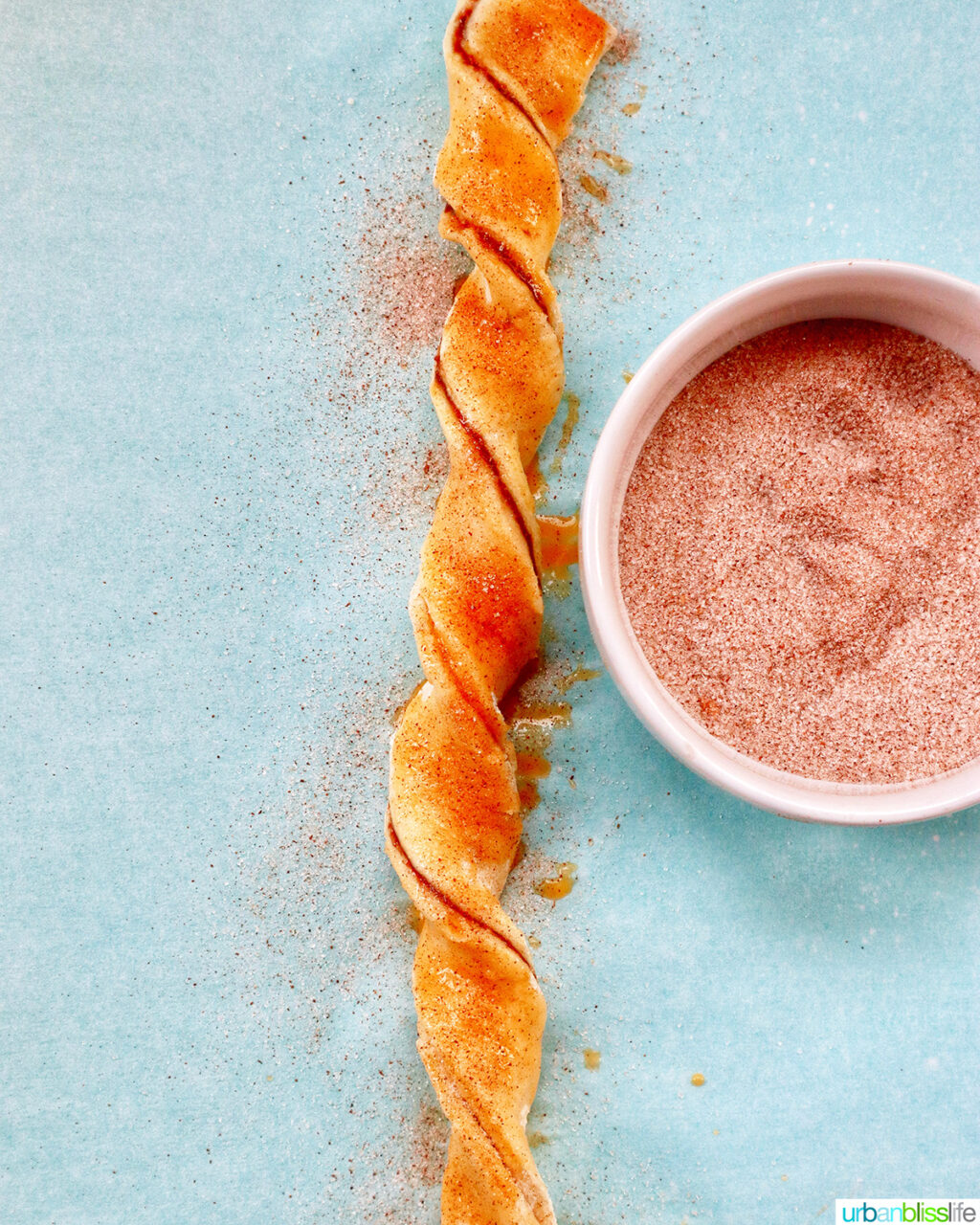 puff pastry chocolate twist on a baking sheet next to bowl of cinnamon sugar.