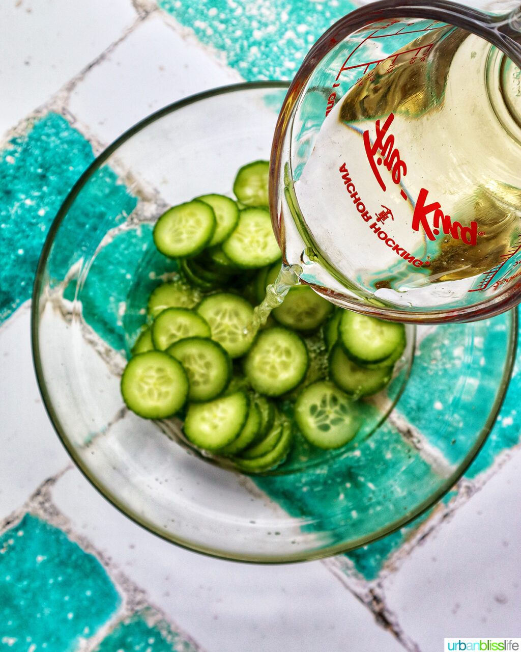 pouring rice vinegar over cucumbers in a bowl.