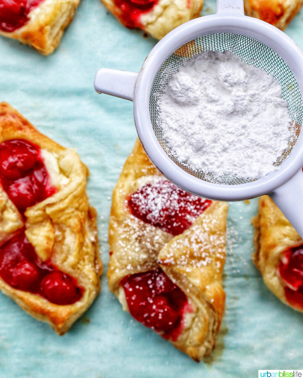 cherry danish pastries on a baking sheet with powdered sugar over it.