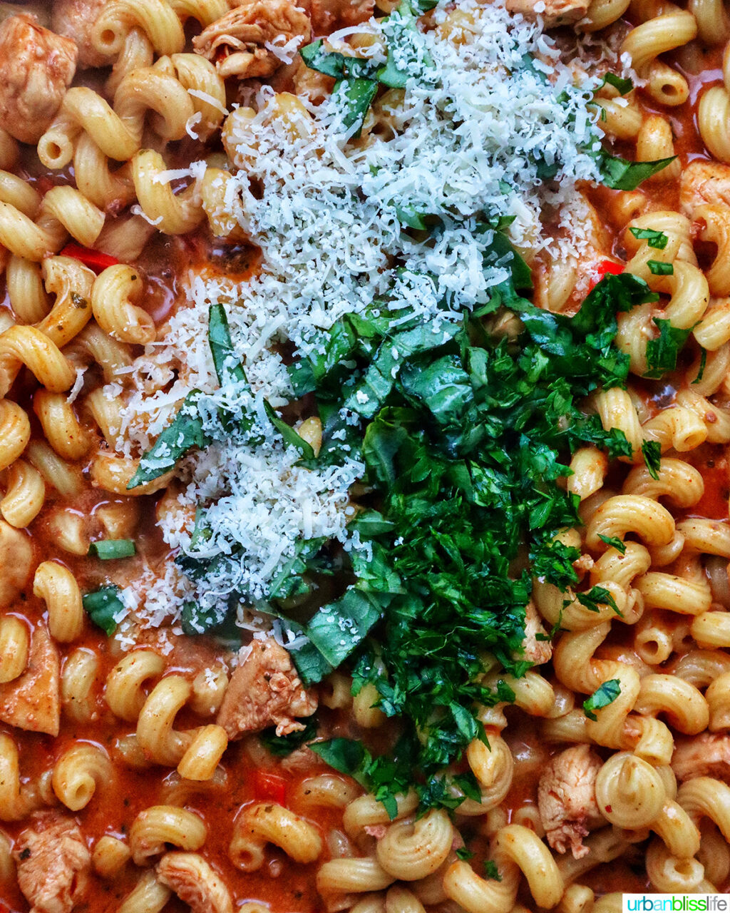 herbs and cheese added to chorizo chicken pasta cooking in a pan.