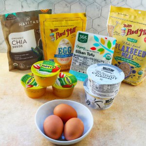 several egg substitutes and egg replacement ingredients plus a bowl of eggs.