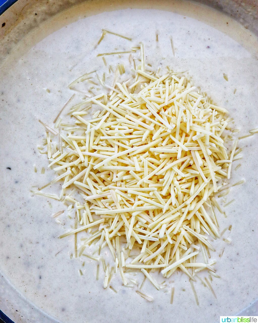 adding shredded cheese to creamy garlic pasta sauce in a pan.