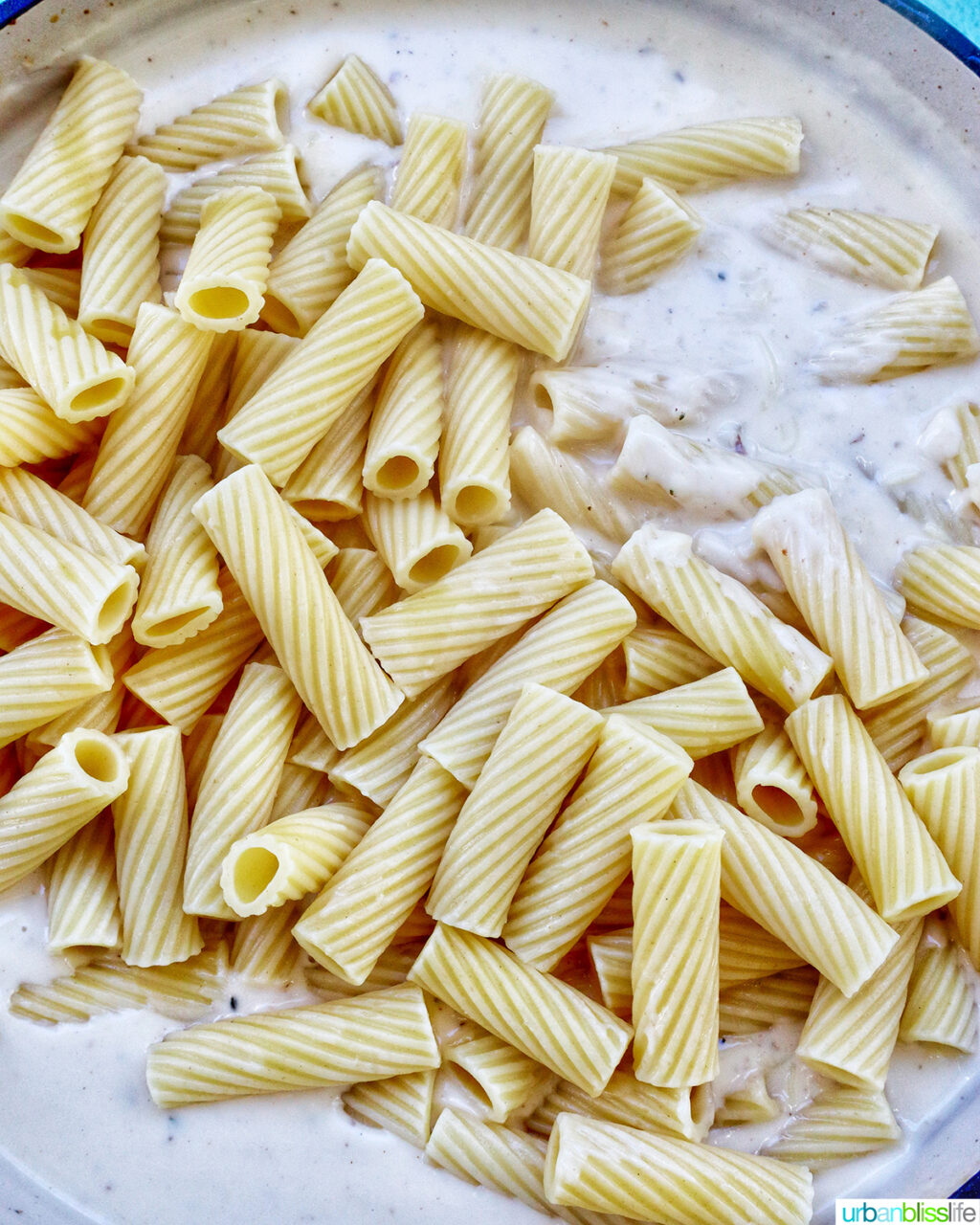 adding pasta to creamy garlic pasta sauce in a pan.