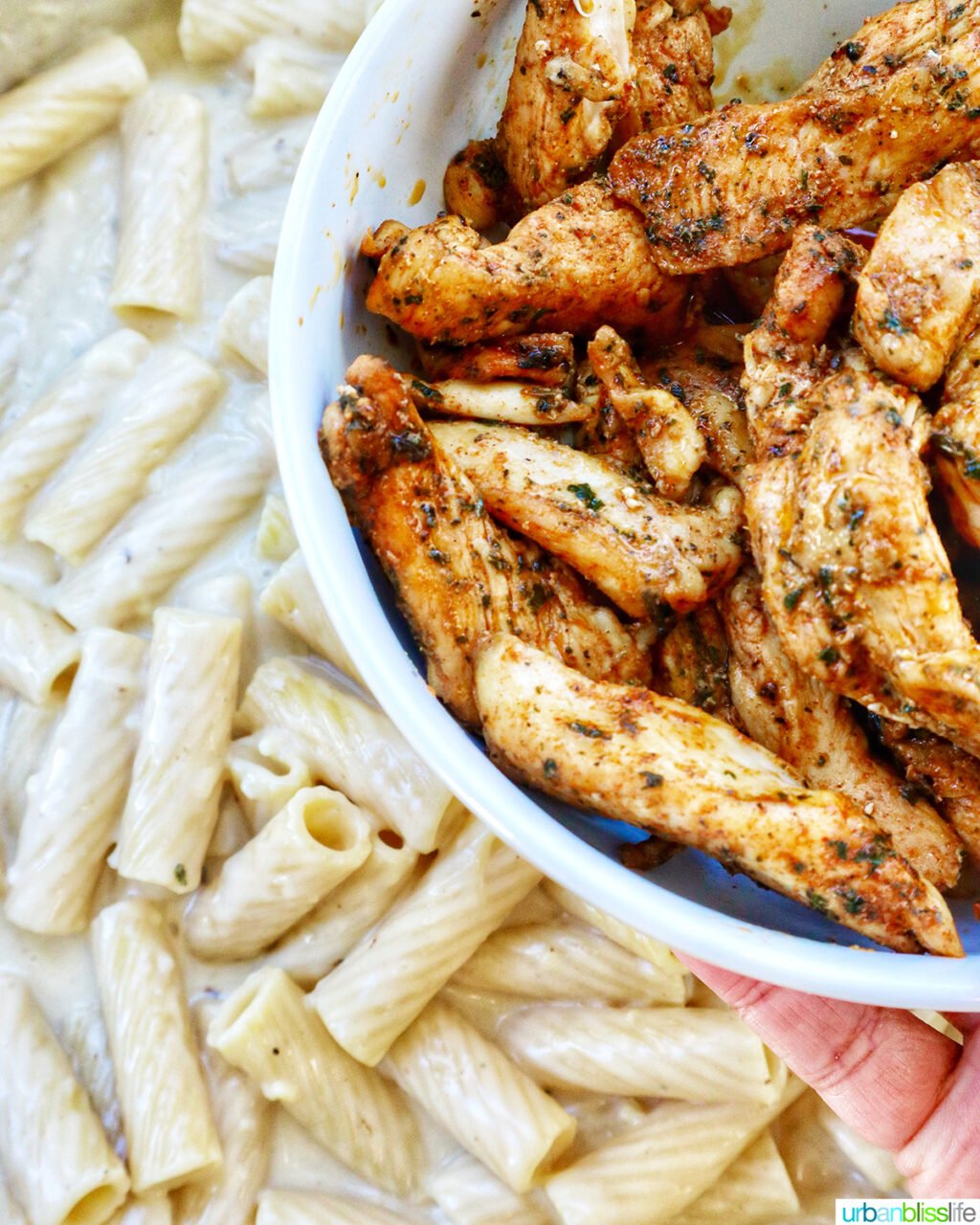 adding chicken to creamy garlic pasta sauce in a pan.