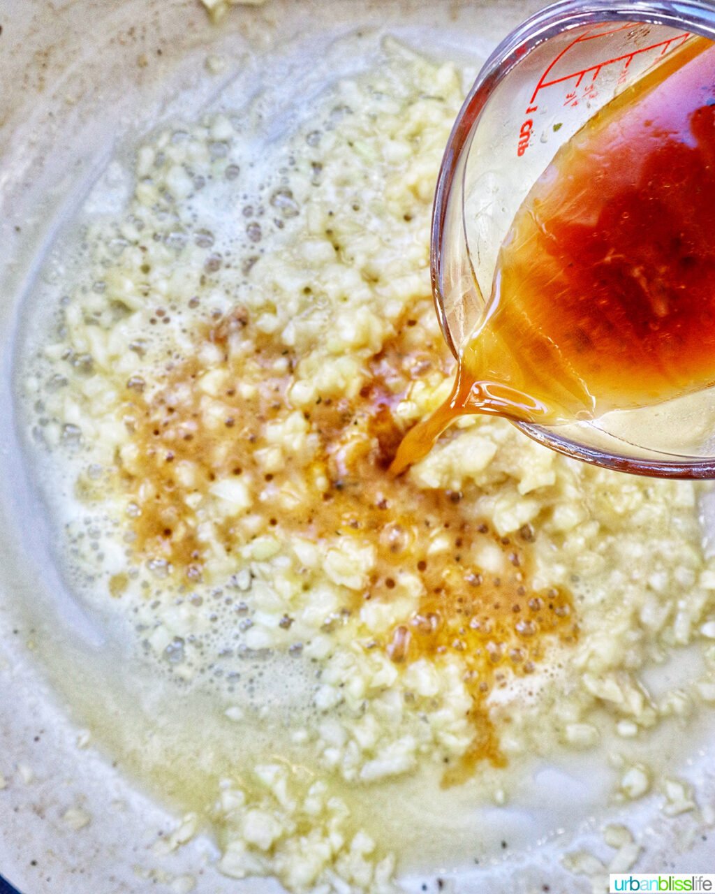 pouring chicken stock over garlic and onions sauteing in butter.