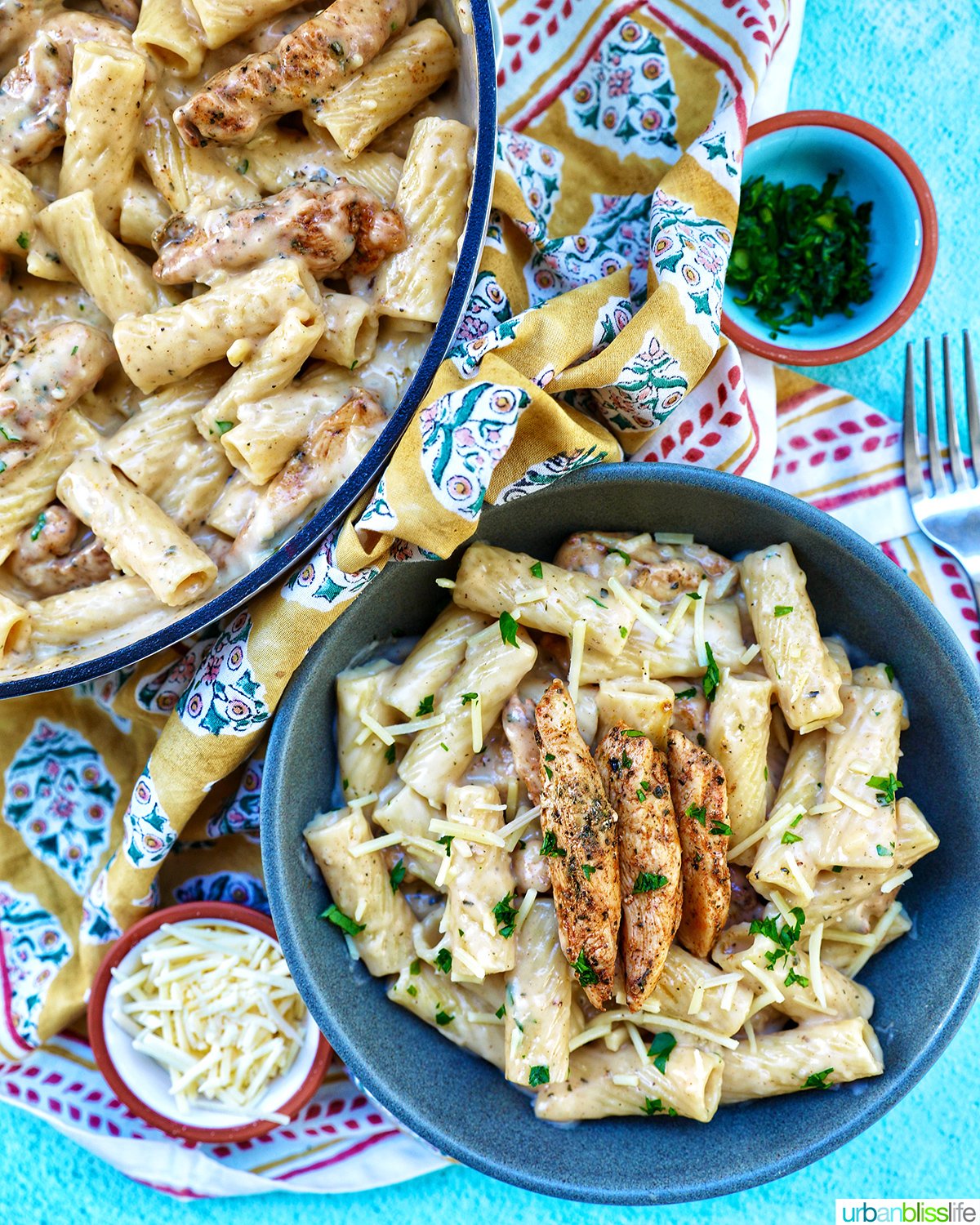 Bowl of garlic chicken parmesan pasta with side bowl of parsley next to pan of pasta.