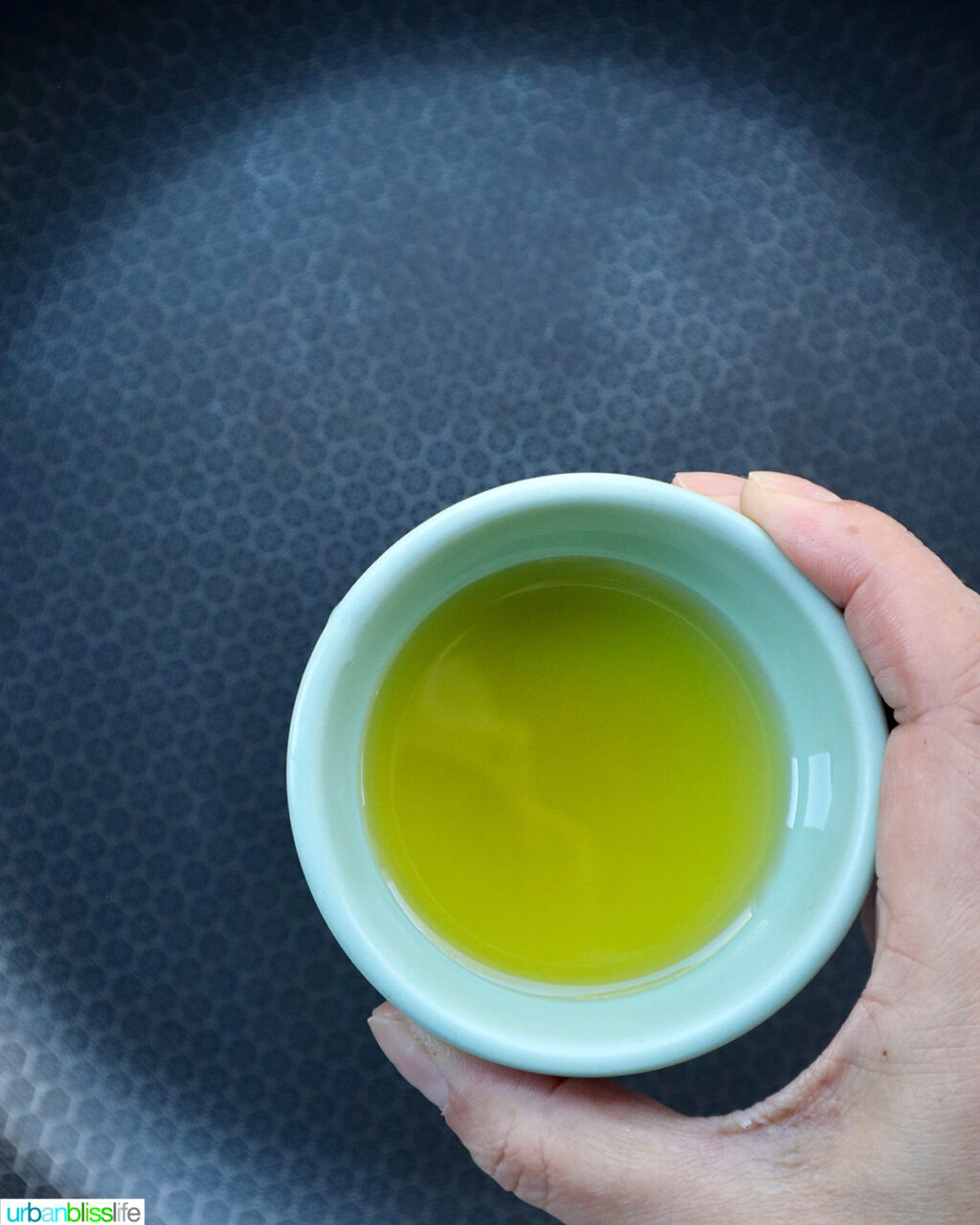 hand holding a bowl of olive oil over a skillet.