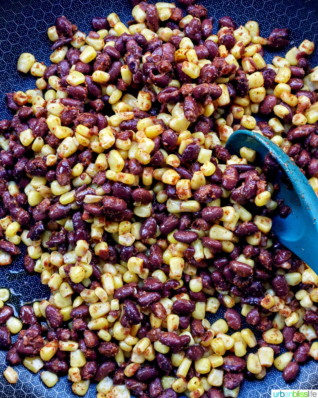 corn, beans and seasoning being stirred in a skillet.