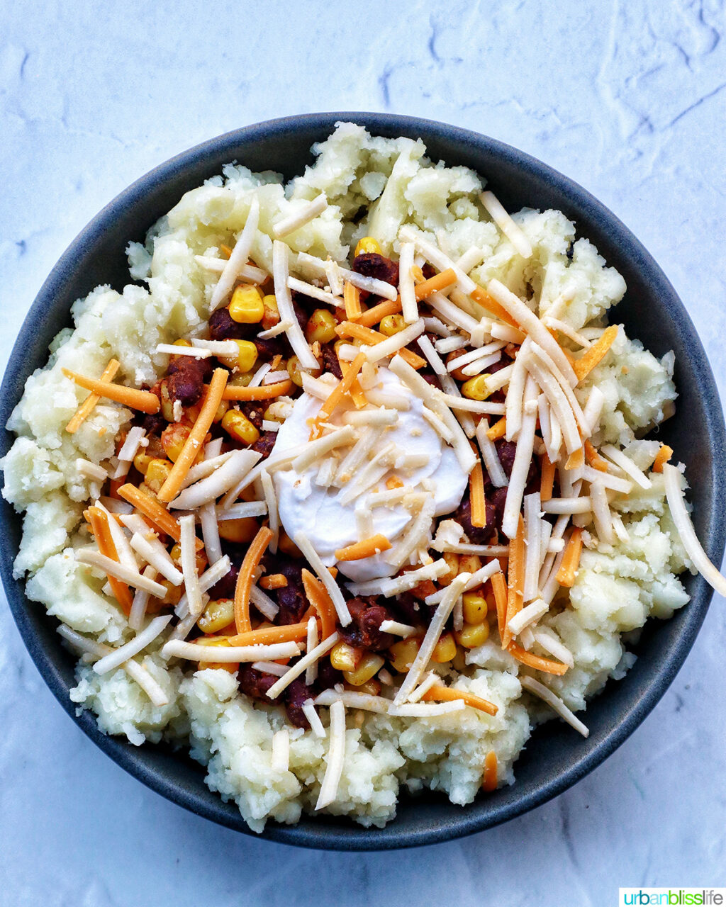 loaded potato bowl with mashed potatoes, beans, corn, cheese, and herbs.