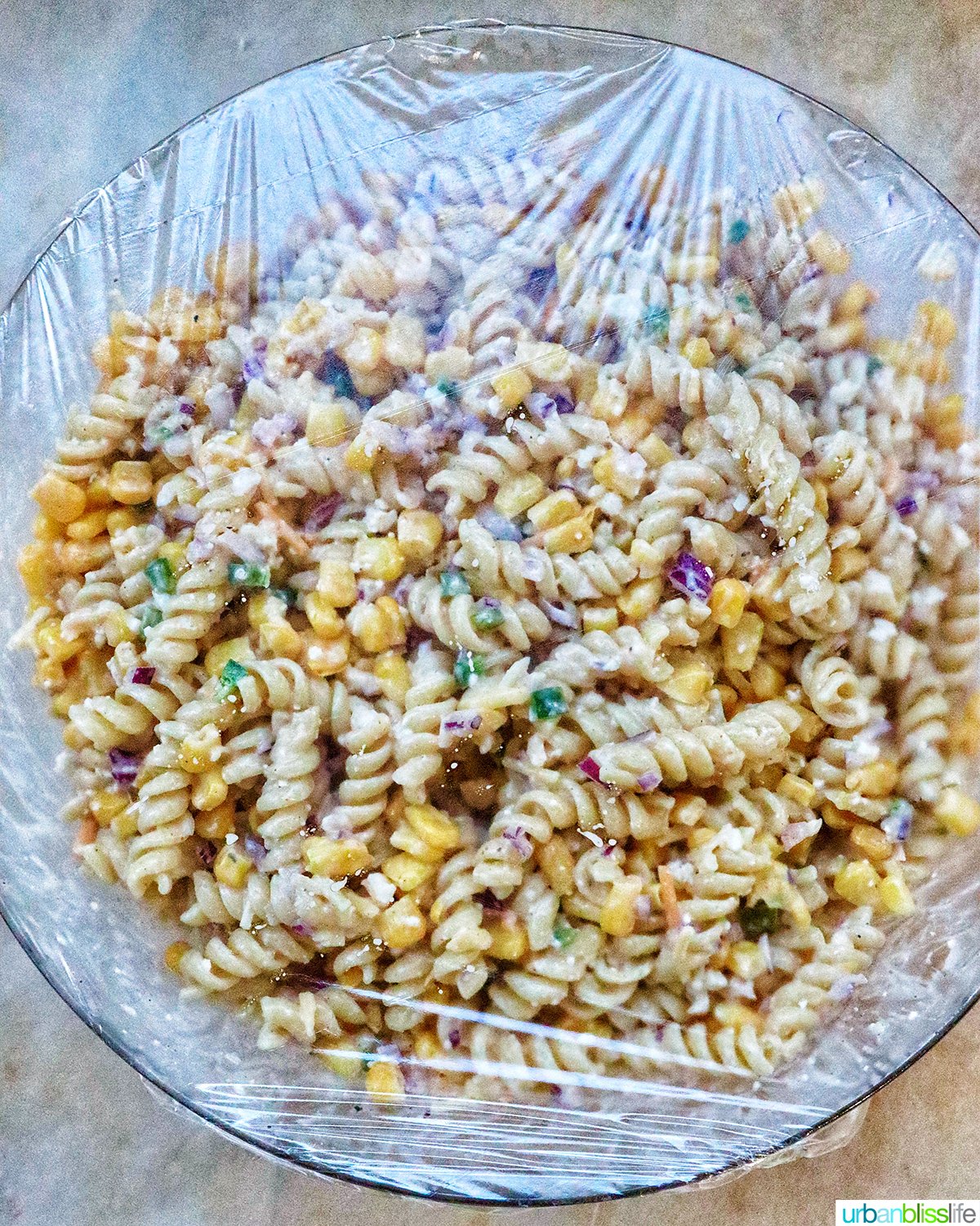 Mexican street corn pasta salad covered with plastic wrap in a bowl.