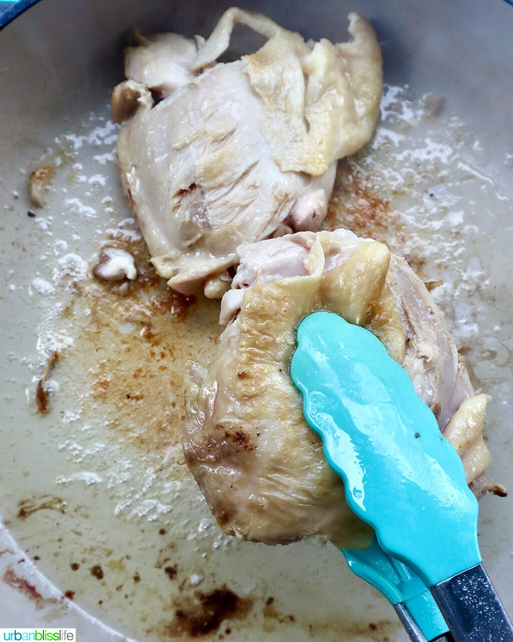 tongs turning chicken thighs over in a skillet.