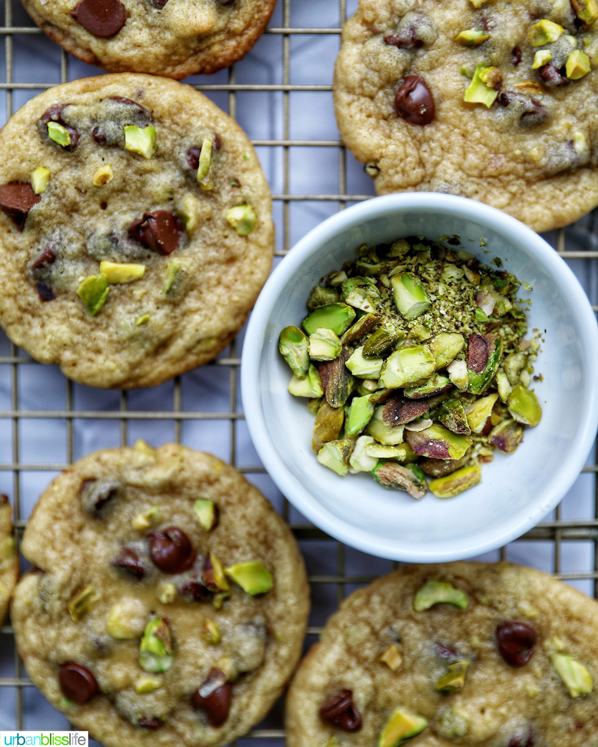 chocolate chip pistachio cookies on a cooling rack with a bowl of pistachios.