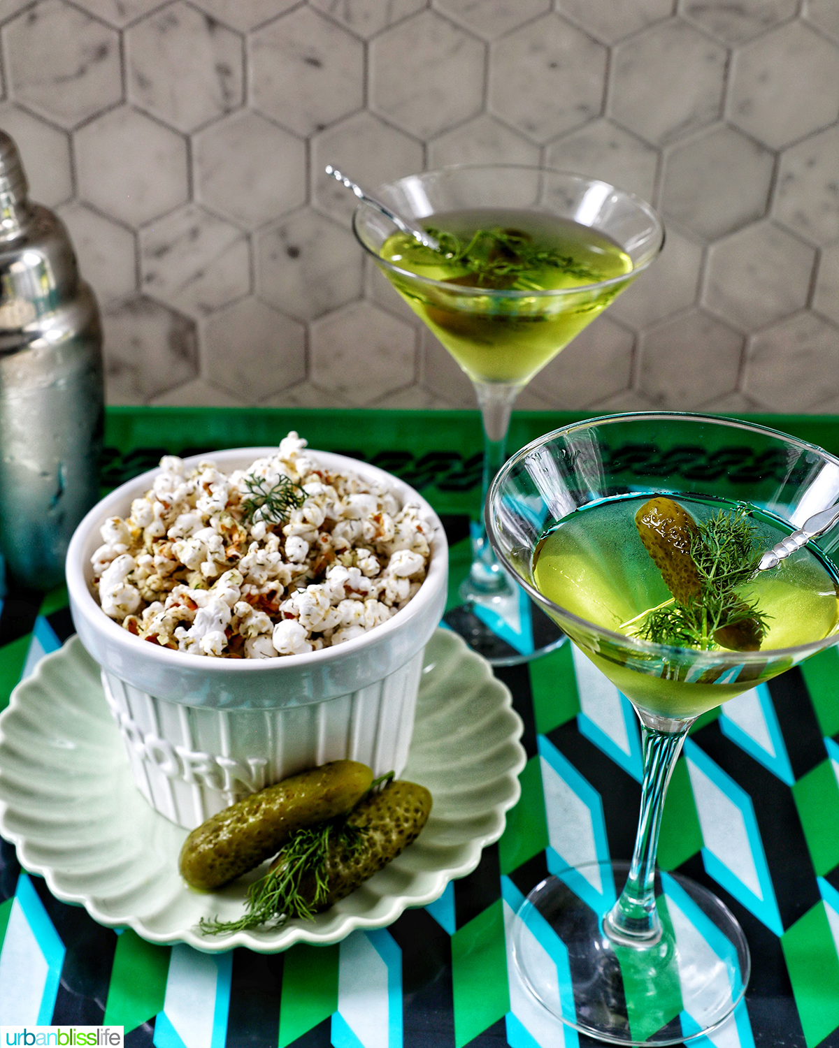 two dill pickle martinis next to a bowl of of dill pickle popcorn.