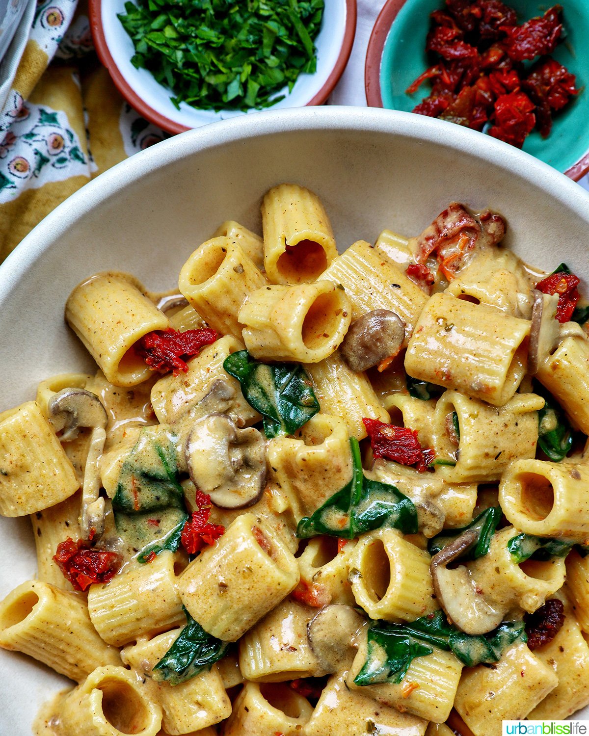 bowl of Marry Me Pasta with bowls of parsley and sun-dried tomatoes.