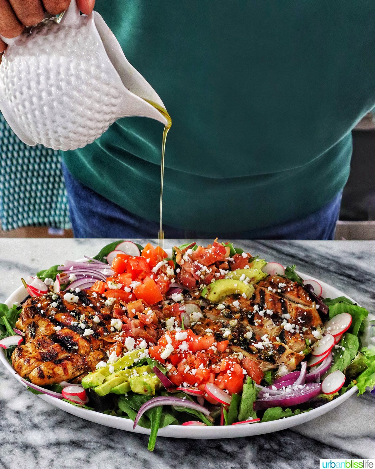 pouring dressing over a platter of Balsamic Chicken Salad.