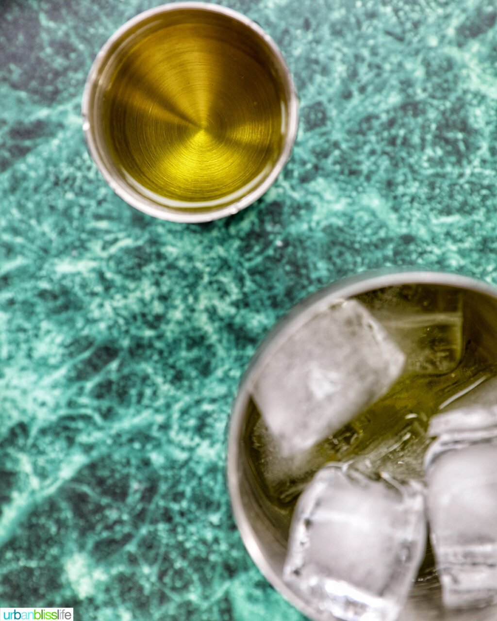 pickle juice in a cocktail jigger above a cocktail shaker of ice.