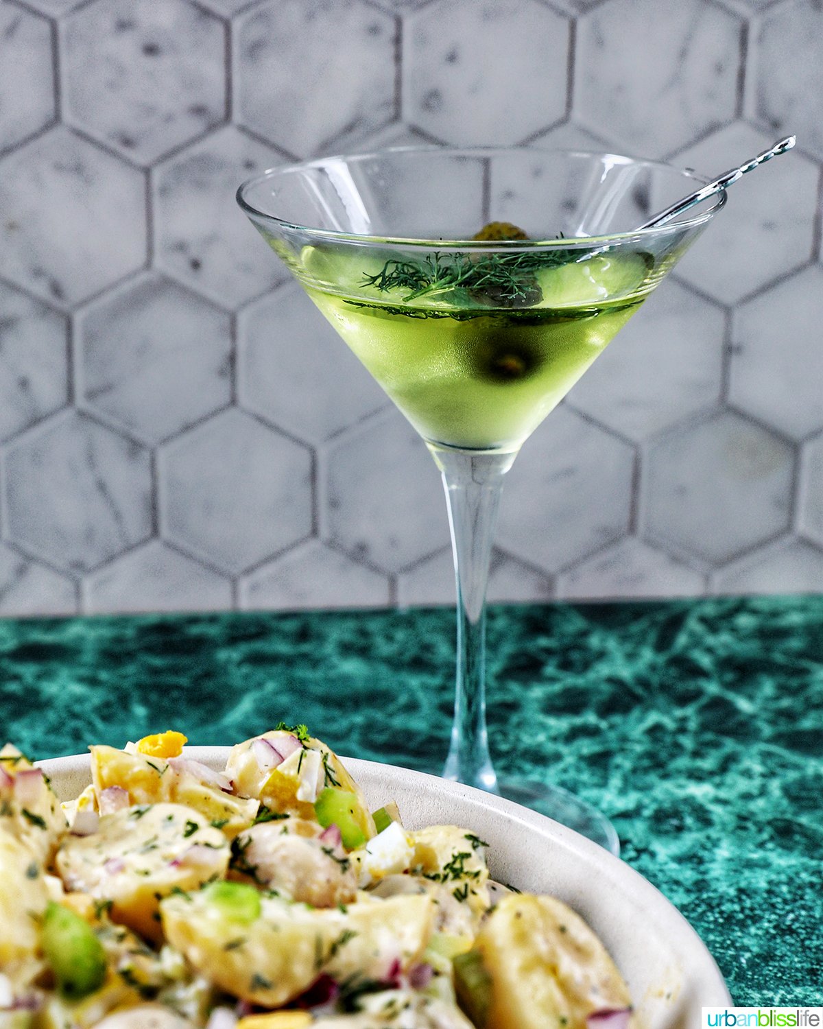 glass of dill pickle martini with a bowl of dill pickle potato salad.