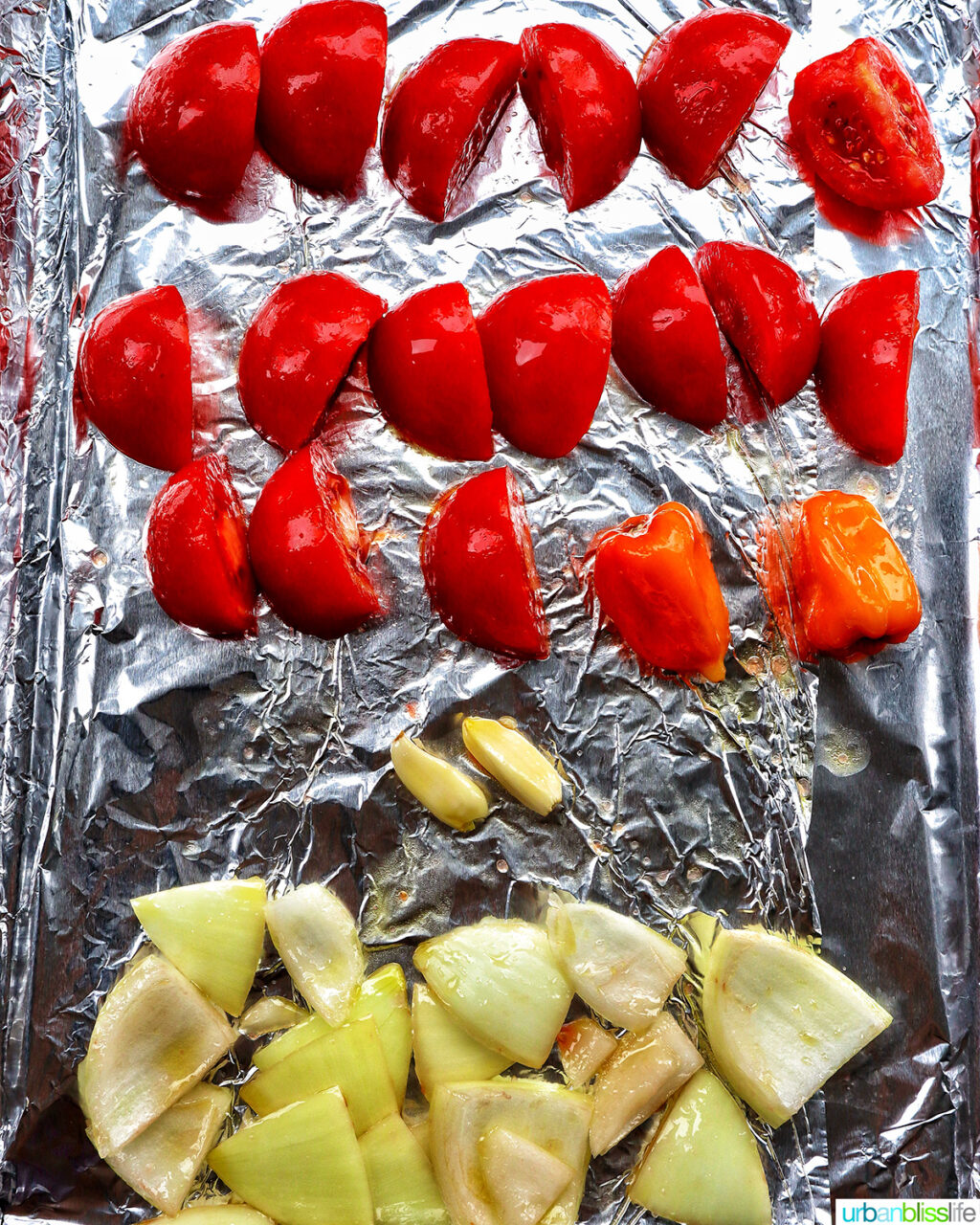sliced tomatoes, onions, habanero, and garlic on a baking sheet for roasting.