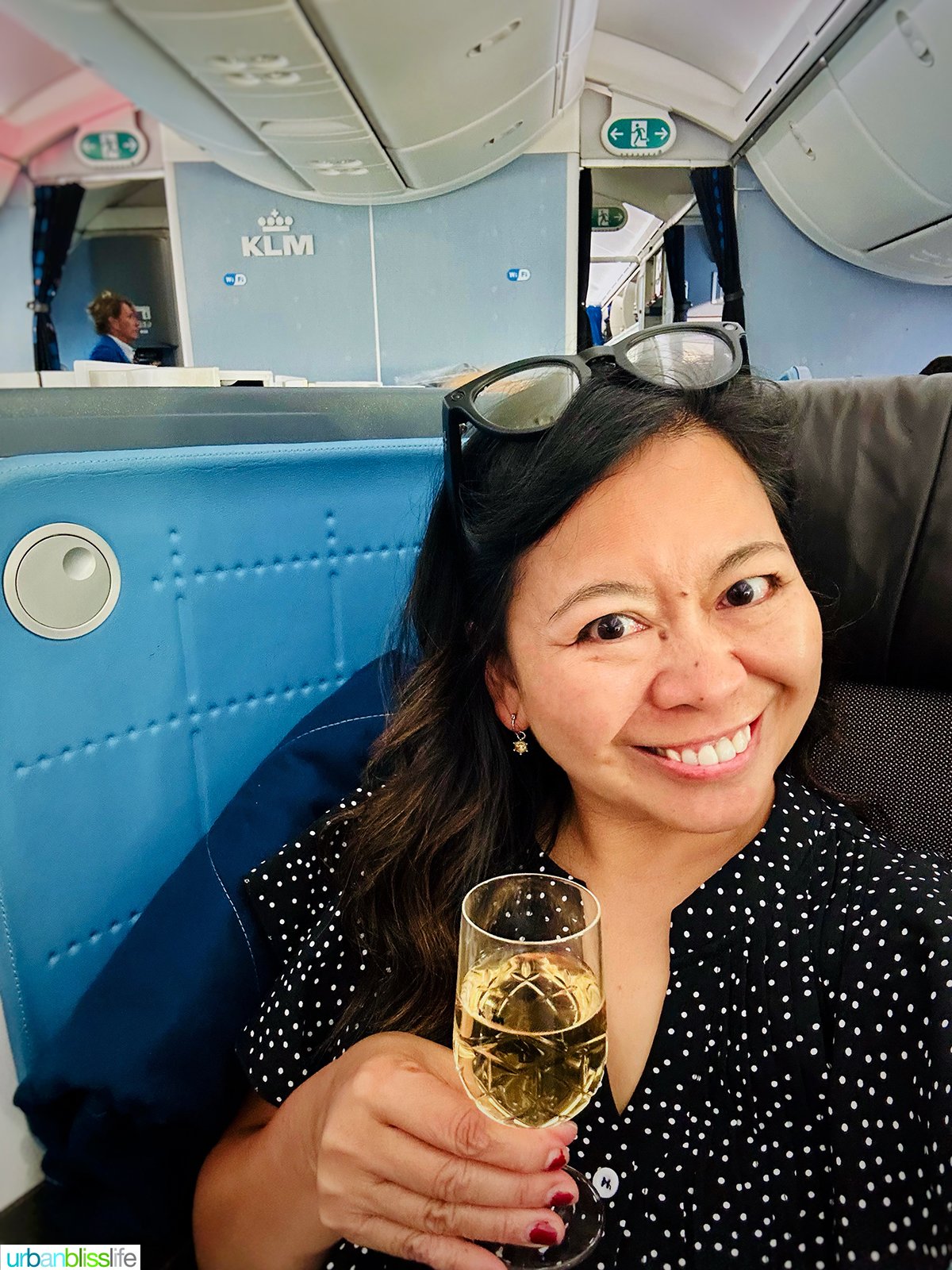 Marlynn Jayme Schotland holding a glass of champagne in KLM airlines business class.