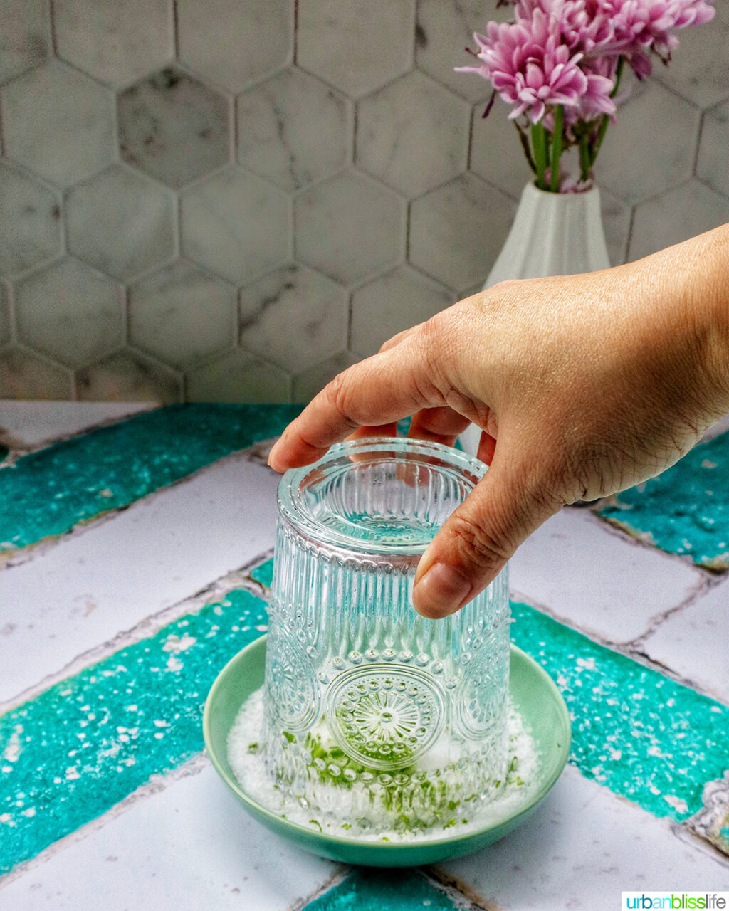 hand holding a cocktail glass over a shallow bowl of lime salt.