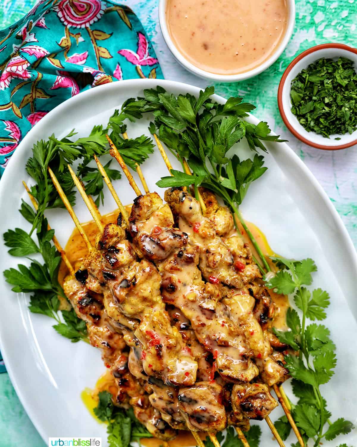 bang bang chicken skewers on a plate with sides of sauce and garnish.