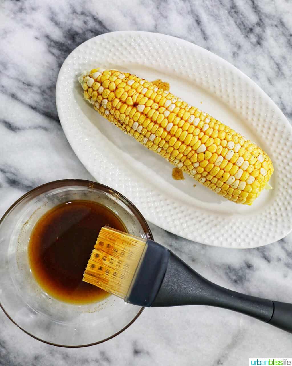 basting brush with marinade and corn on the cob.