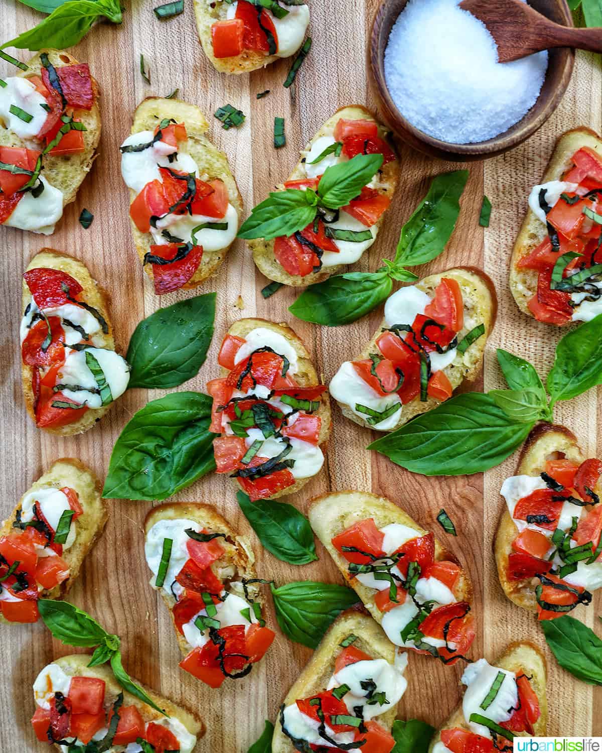 lots of crostini pizzas on a wooden board with a side bowl of salt.