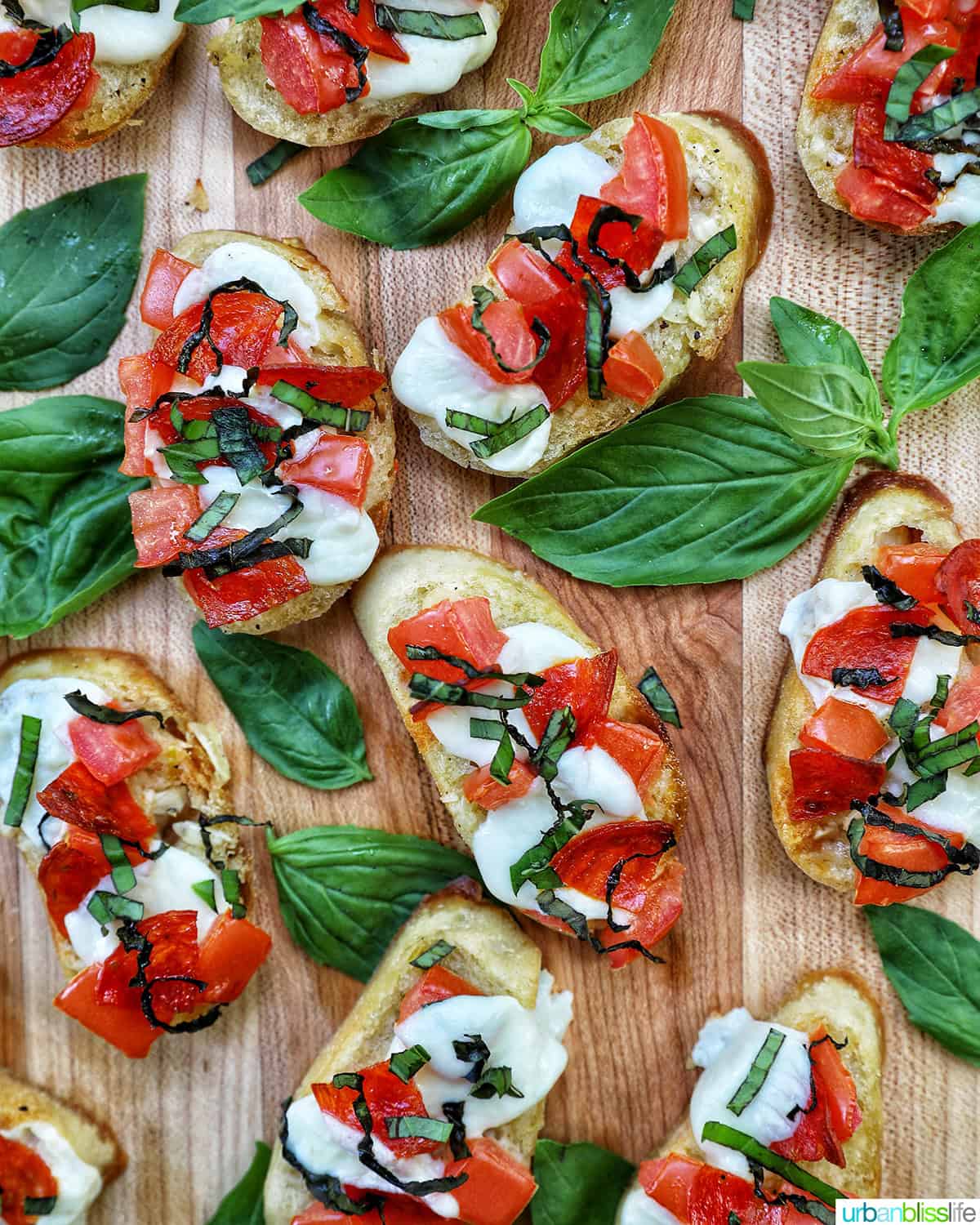 lots of crostini pizzas on a wooden board with a side bowl of salt.