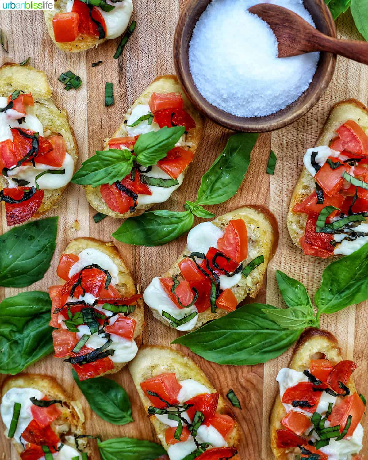 lots of crostini pizzas on a wooden board with a side bowl of salt.