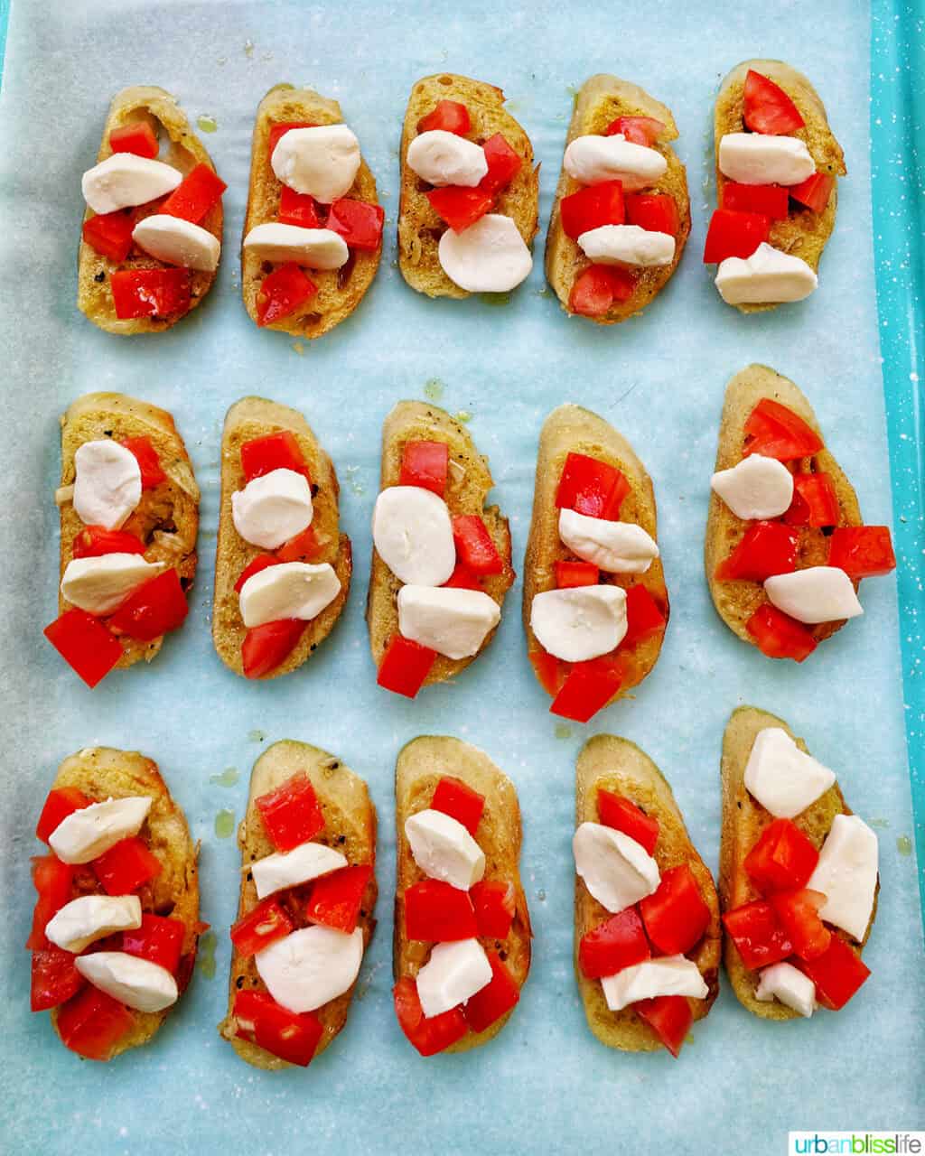 sliced crostini on a baking sheet topped with tomatoes and cheese.