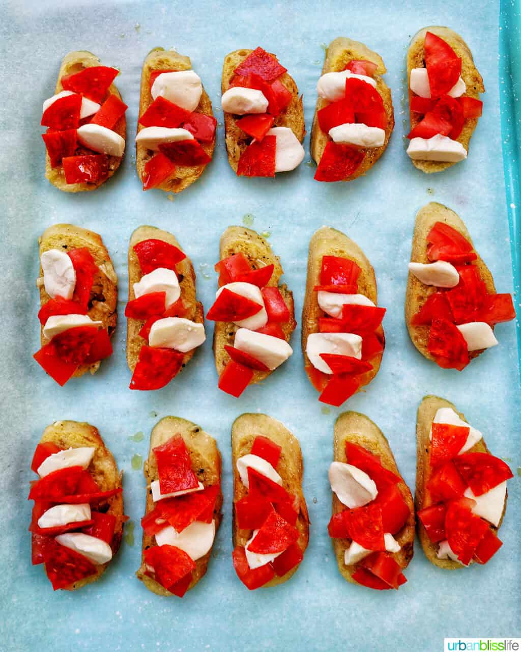 sliced crostini on a baking sheet topped with tomatoes, pepperoni, and cheese.
