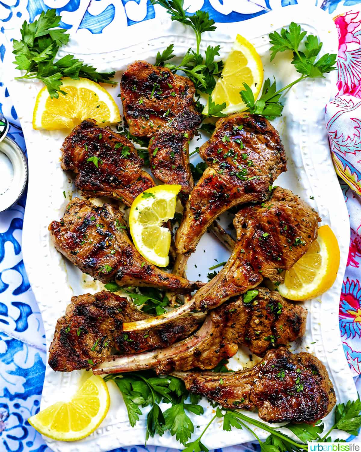 Greek lamb chops on a white plate with herbs and lemon slices.