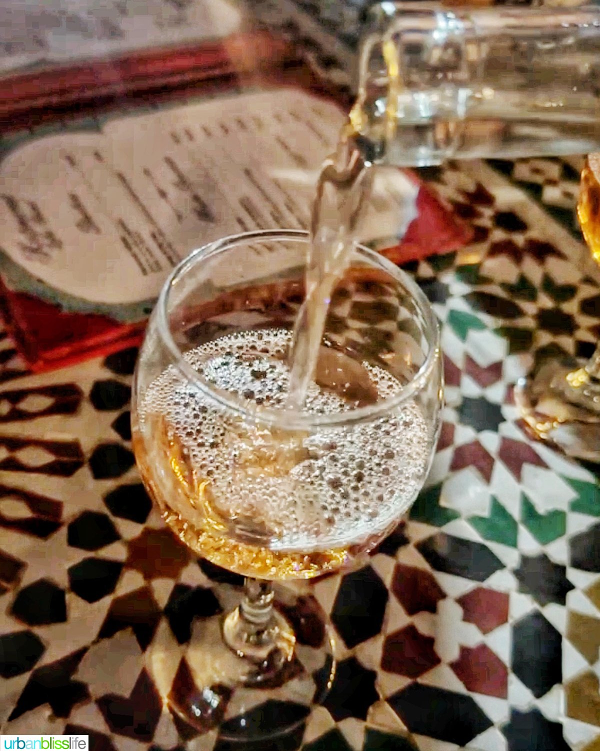 pouring Moroccan rosé wine into a glass on top of Moroccan tile.