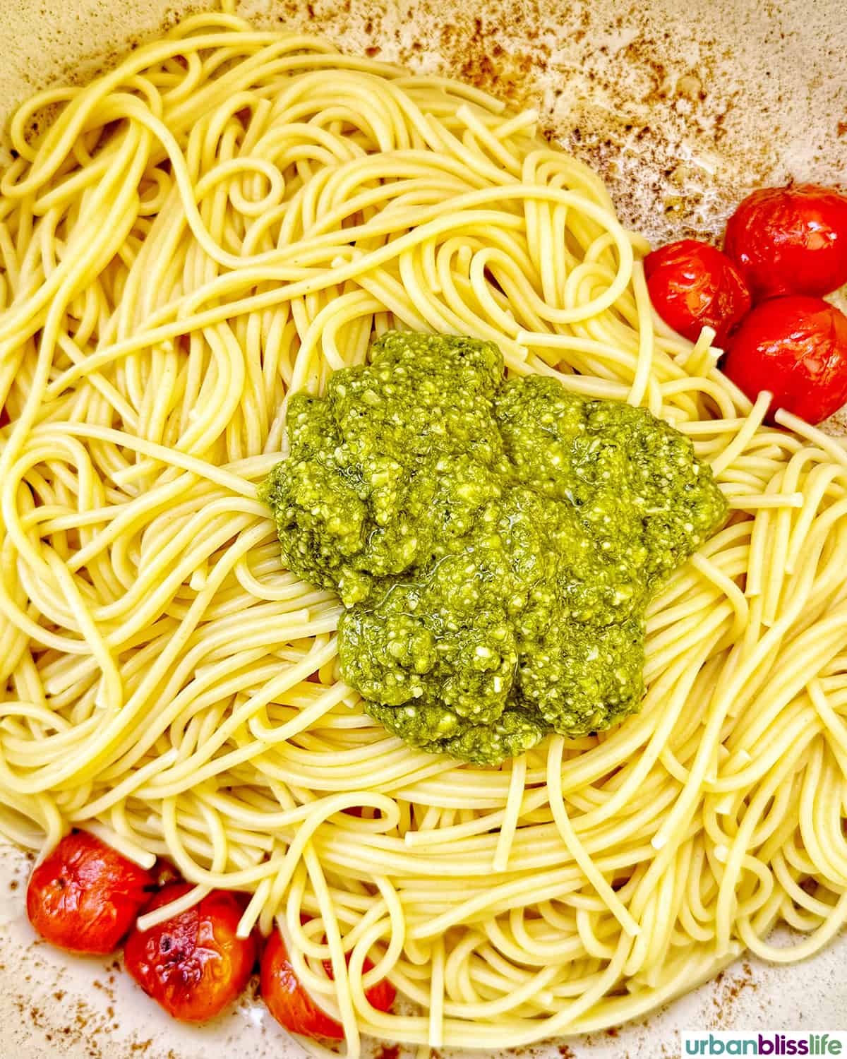 pesto added to spaghetti pasta with cherry tomatoes in a pan.