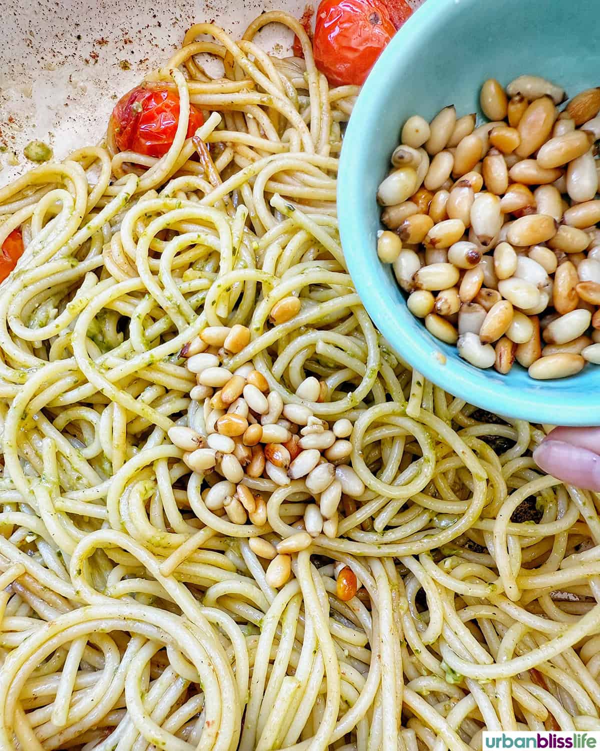 pine nuts added to pesto and spaghetti pasta with cherry tomatoes in a pan.