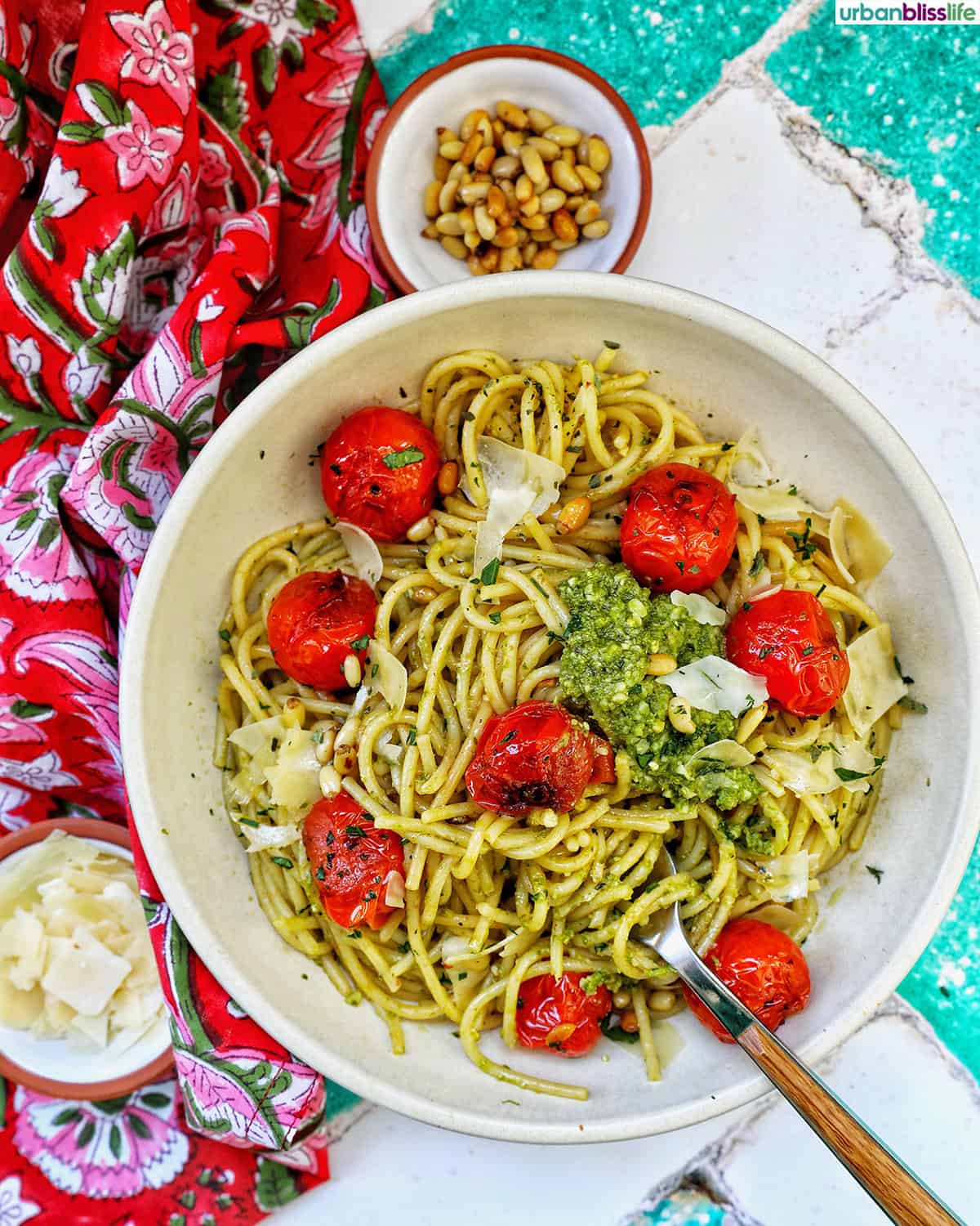 bowl of cherry tomato and pesto pasta and bowls of pine nuts and cheese.